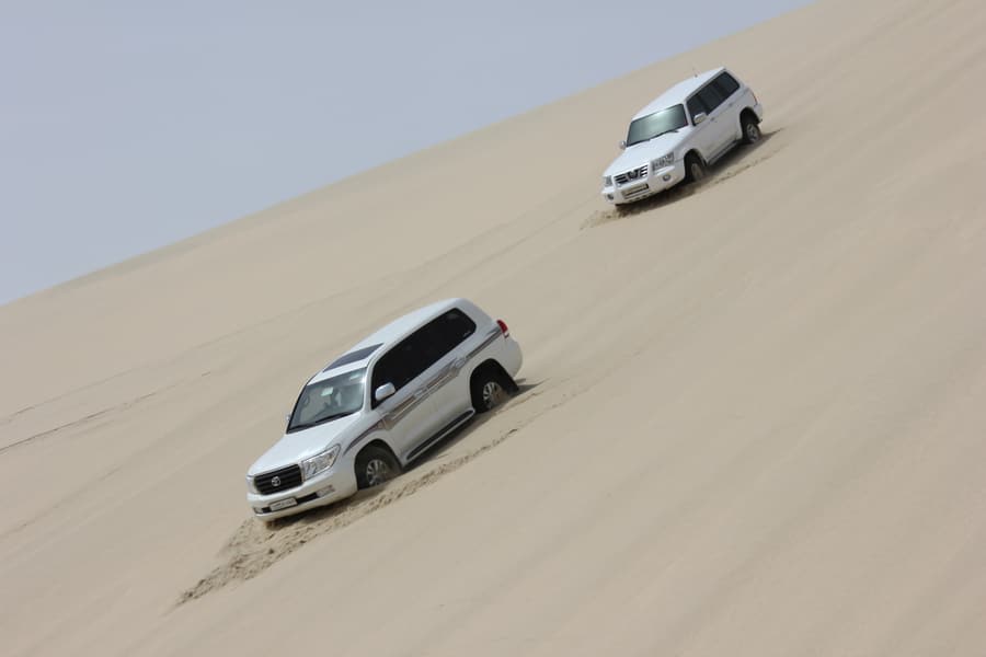 4x4 vehicles driving down a steep sand dune